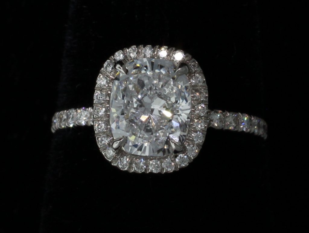 Platinum Jewelry - A large circular cut diamond surrounded by smaller diamonds in a platinum setting.